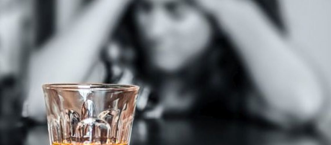 Alcohol addiction : Portrait of a lonely and desperate drunk hispanic woman (image focused on her drink)